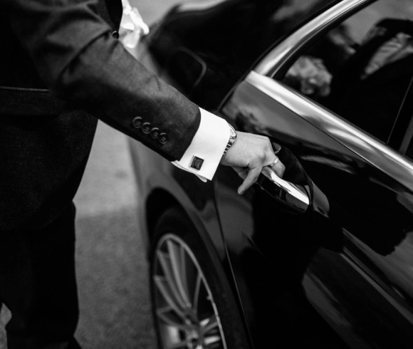 A chauffeur in a suit opening the door of a black luxury car.