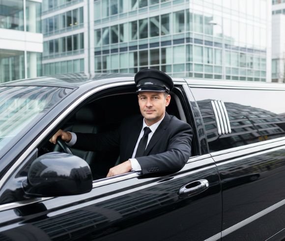 Professional chauffeur sitting in front seat of stretch limousine outside glass office building Professional chauffeur sitting in front seat of stretch limousine outside glass office building.