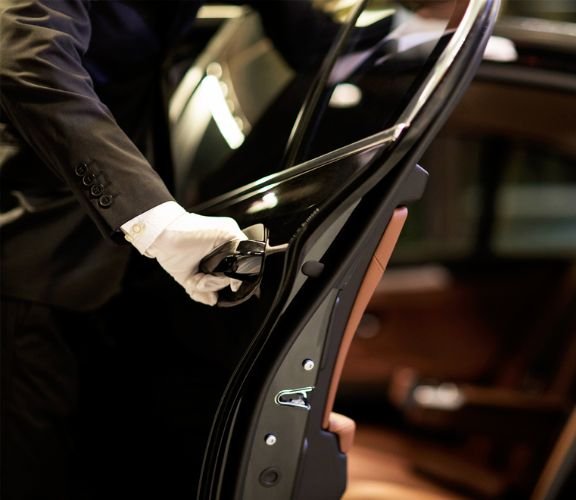 A chauffeur in white gloves opening the door of a luxurious limo.