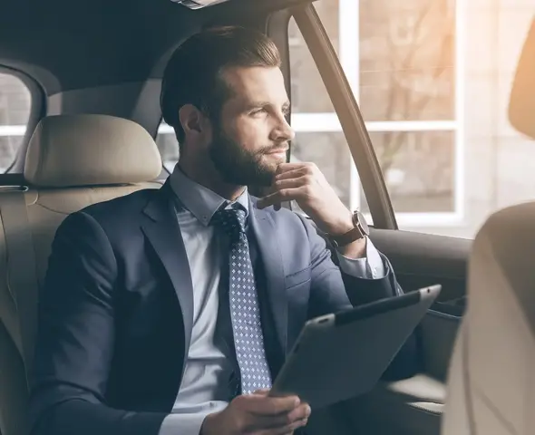 executive-airportcar-service Man in a suit holding a tablet in the backseat of a luxury car.