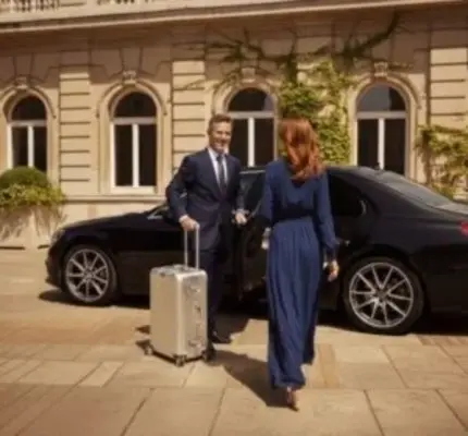 Chauffeur assisting passenger beside luxury sedan outside elegant building. Chauffeur assisting passenger beside luxury sedan outside elegant building.